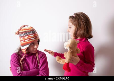 Gieriges Kinderkonzept. Beziehungen der Schwestern. Teile Spielzeuge mit Freunden. Kinder auf weißem Hintergrund spielen mit Spielzeug Stockfoto