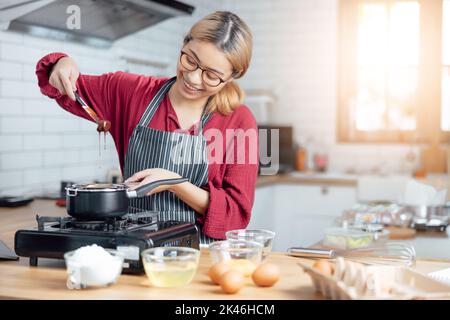 Schöne junge Frau mischt Teig, Blick auf die Kamera und lächelt beim Backen in der Küche zu Hause, Dekoration einen Kuchen aus Schokoladenkuchen, Kochen cl Stockfoto