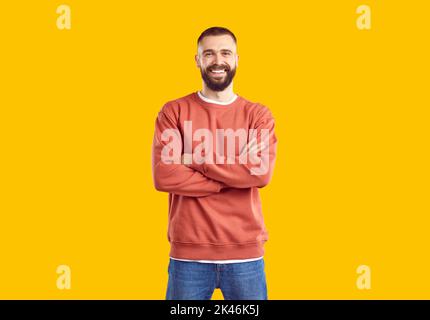 Ein junger lächelnder Mann in rotem Sweatshirt und Jeans posiert auf gelbem Hintergrund und blickt auf die Kamera. Stockfoto