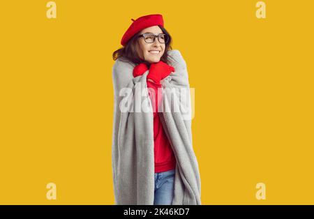 Frau in Brille, roten Handschuhen und Hut eingewickelt in karierte vor Kälte auf gelbem Hintergrund gedrängt. Stockfoto