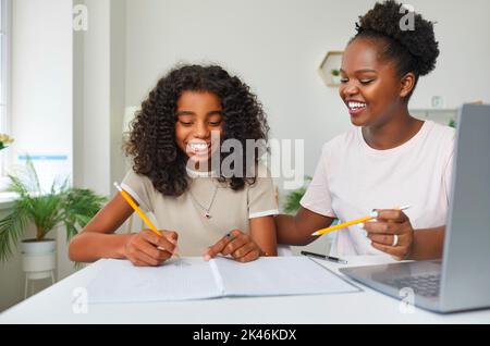 Die fürsorgliche und freundliche Mutter hilft ihrer Tochter, Hausaufgaben zu machen, die in der Schule zugewiesen wurden. Stockfoto