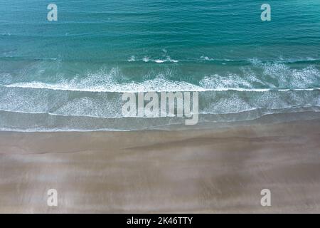 Drone-Ansicht von oben auf das türkisfarbene Meer und die weiß getünchte Wellen, die an einem leeren goldenen Sandstrand brechen Stockfoto