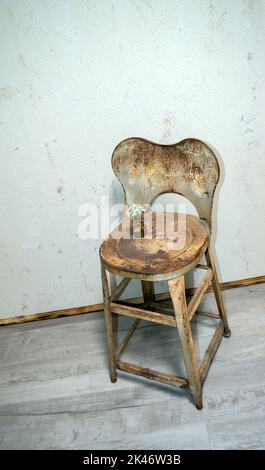 Ein alter Stil Bauernhaus Distressed Metall Stuhl wird verwendet, um eine niedliche kleine weiße Blumenarrangement in einer winzigen Bär förmigen Vase zu platzieren. Ein abgenutzter Hintern Stockfoto