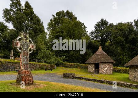 Wexford, Irland - 18. August 2022: Blick auf ein frührekonstruiertes christliches Kloster im Irish National Heritage Park mit einem großen keltischen Kreuz i Stockfoto