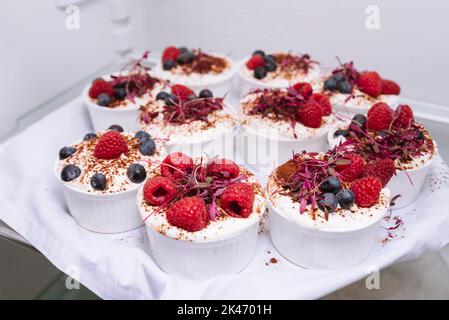 Desserts auf einem Tablett im Kühlschrank. Weiße Ramekins mit gekühlten Desserts mit Beeren. Himbeeren, Heidelbeeren, Kakaopulver. Stockfoto