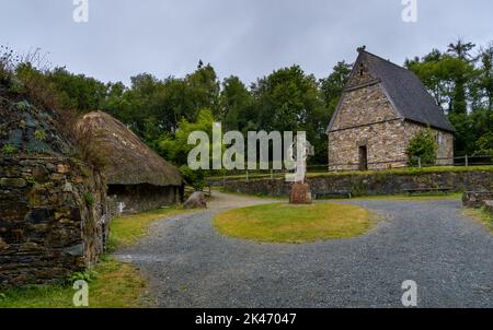 Wexford, Irland - 18. August 2022: Blick auf ein frührekonstruiertes christliches Kloster im Irish National Heritage Park mit einem großen keltischen Kreuz i Stockfoto