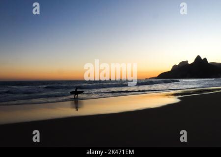 Rio de Janeiro, RJ, Brasilien, 2022 - Ein Surfer in Silhouette Spaziergänge am Strand von Ipanema bei Sonnenuntergang Stockfoto