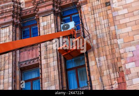 Kommunale Servicemitarbeiter in orangefarbenen Uniformen auf einer mobilen Luftplattform reparieren die festlichen elektrischen Girlanden des neuen Jahres. Stockfoto