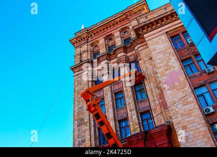 Kommunale Servicemitarbeiter in orangefarbenen Uniformen auf einer mobilen Luftplattform reparieren die festlichen elektrischen Girlanden des neuen Jahres. Stockfoto