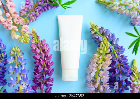 Mockup weiße Squeeze-Flasche Kosmetikschlauch und Lupinenblumen auf blauem Hintergrund. Creme, Gleitgel, Feuchtigkeitscreme, Hautpflege, Sonnencreme. Flach liegend, oben Stockfoto