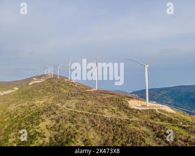 Windturbinen auf schönen sonnigen Sommer Herbst Berglandsland. Kurvige Straße durch den Berg Eolic Park. Grüne ökologische Energieerzeugung Stockfoto