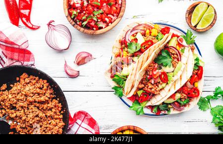 Mexikanische Küche. Tacos mit Rindfleisch, Mais, roten Bohnen, Tomatensalsa-Sauce und Zwiebeln in Mais-Tortilla auf dem Teller. Weißer Tischhintergrund, Draufsicht Stockfoto