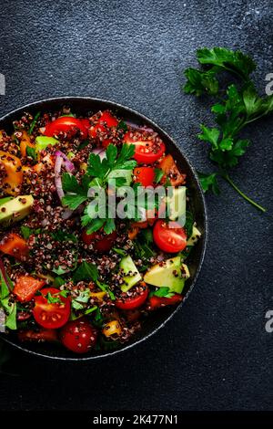 Quinoa Tabbouleh Salat mit Tomaten, Paprika, Avocado, Gurken, Zwiebeln und Petersilie. Traditionelles nahöstliches und arabisches Gericht. Schwarzer Küchentisch Stockfoto