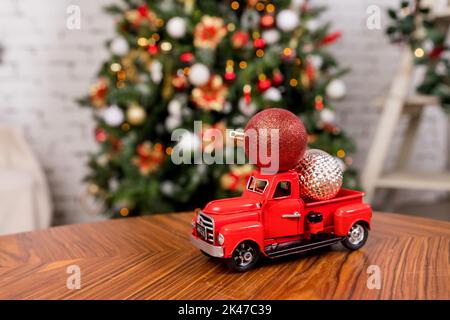 Rotes Auto trägt einen Weihnachtsschmuck auf dem weihnachtsbaum Hintergrund. Spielzeug-LKW über festlichen Hintergrund.Konzept für Winterferien. Speicherplatz kopieren Stockfoto