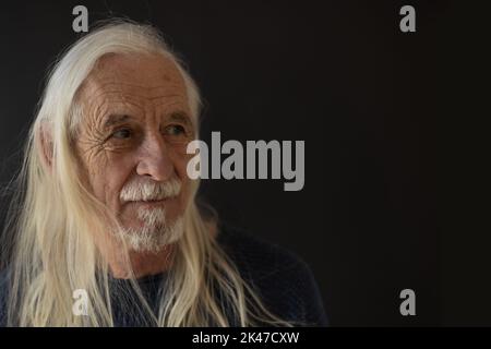 Lächelnder, schöner alter Mann - Rockfan - posiert mit grauem, langem Haar. Horizontal. Stockfoto