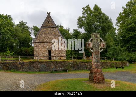 Wexford, Irland - 18. August 2022: Blick auf ein frührekonstruiertes christliches Kloster im Irish National Heritage Park mit einem großen keltischen Kreuz i Stockfoto