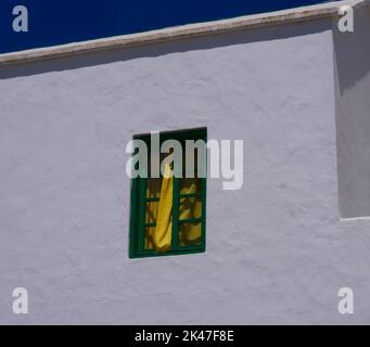 Weiße Hauswand mit grünem Fenster und gelbem Vorhang Stockfoto