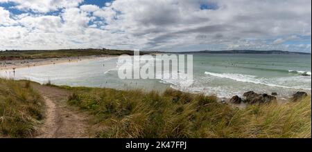 Panoramalandschaft eines sandigen Fußweges, der durch Sanddünen zum Gwihian Beach führt, mit vielen Strandbesuchern und Surfern im Wasser an einem schönen späten Abend Stockfoto