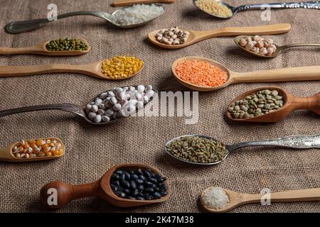 Vegane Proteinquelle. Verschiedene Arten von Hülsenfrüchten, Linsen, Kichererbsen und Bohnen in verschiedenen Löffeln auf Holztisch. Draufsicht. Stockfoto