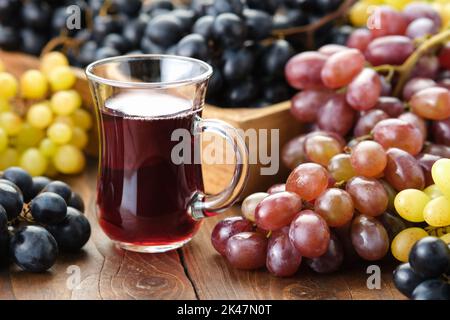 Eine Tasse Traubensaft oder Wein. Schwarze, grüne und violette Trauben auf dem Tisch. Stockfoto