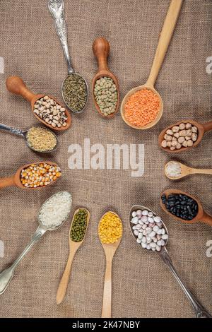 Vegane Proteinquelle. Verschiedene Arten von Hülsenfrüchten, Linsen, Kichererbsen und Bohnen in verschiedenen Löffeln auf Holztisch. Draufsicht. Stockfoto