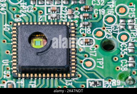 Grüner Silizium-Chip und goldene Drähte in der runden Bohrung des integrierten Schaltkreises. Nahaufnahme des optoelektronischen Sensors auf der Leiterplatte von der Maus des optischen Lasercomputers. Stockfoto