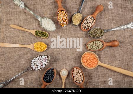 Vegane Proteinquelle. Verschiedene Arten von Hülsenfrüchten, Linsen, Kichererbsen und Bohnen in verschiedenen Löffeln auf Holztisch. Draufsicht. Stockfoto