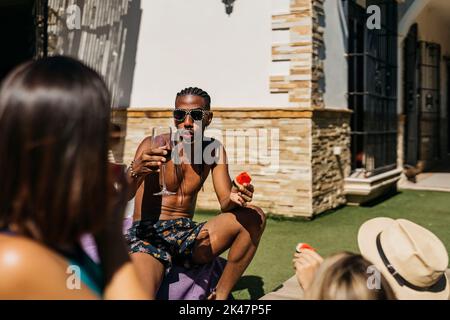Junger schwarzer Mann mit Dreadlocks, der Wassermelone isst und im Urlaub mit Freunden spricht Stockfoto