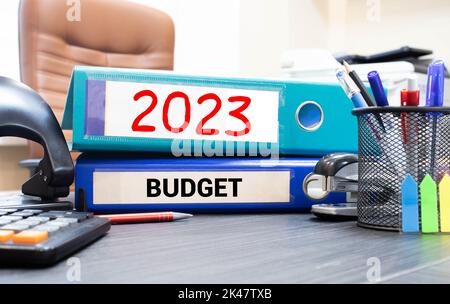 Notizblock mit Text BUDGET 2023, Brille, Büroklammern, weißem Taschenrechner und Stift auf Desktop, Draufsicht. Stockfoto