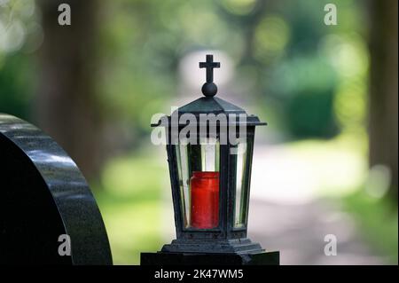 Altmodische Grablaterne mit Kreuz auf einem Grabstein vor verschwommenem Hintergrund Stockfoto