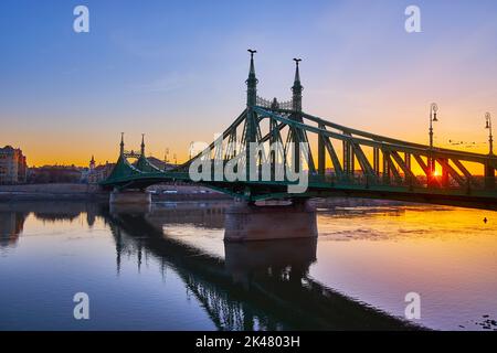 Der helle Sonnenaufgang über der Donau durch die Metalldetails der Jugendstil-Freiheitsbrücke, Budapest, Ungarn Stockfoto