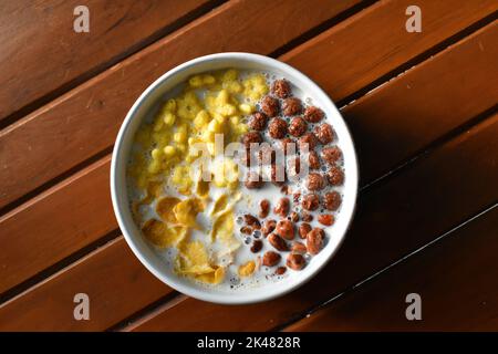 Eine Schüssel Getreide mit Milch auf Holzbank von oben fotografiert. Stockfoto