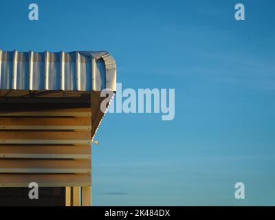 Das Blechdach der Fabrik erhält Sonnenlicht von der Morgensonne. Auf einem Hintergrund, der blauer Himmel ist. Industriekonzept. Stockfoto