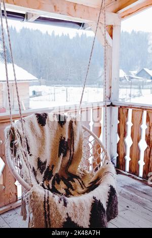 Gemütliche Outdoor-Schaukel auf der Holzterrasse in den Bergen Ferienhaus im Winter Stockfoto