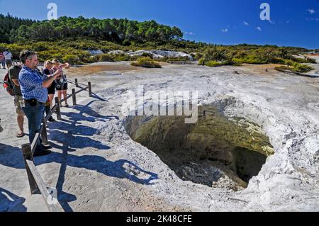 Besucher stehen hinter einer abgehebelten Sicherheitsbarriere an einem Krater namens Devils Home im Wai-O-Tapu Thermal Wonderland in der Nähe der am See gelegenen Stadt Rotorua o Stockfoto