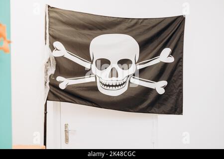 Schwarze Piratenfahne mit Totenkopf und Kreuzknochen an einer weißen Tür. Halloween-Dekor Stockfoto