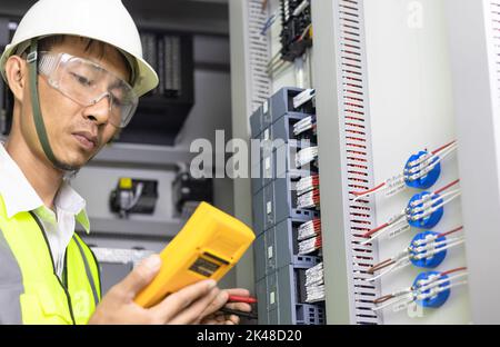 Ein Elektriker arbeitet in einer Schalttafel, einem elektrischen Klemmenkasten. Bedienfeld mit Magnetschütz und Überlastrelais, Messung der Spannung an ma Stockfoto