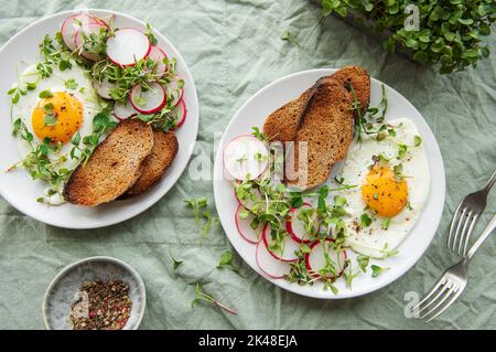 Köstliches Gourmet-Frühstück. Roggenbrot mit Spiegelei, frisch gemahlenem Pfeffer und Salat mit Aufgang und Microgreens. Gesunde Ernährung. Stockfoto