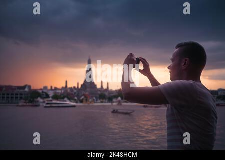Mann beim Fotografieren mit dem Handy gegen den Tempel Wat Arun. Tourist in Bangkok, Thailand. Stockfoto