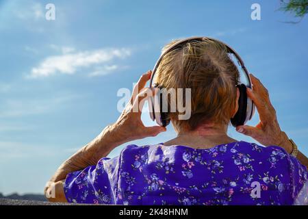 Nahaufnahme einer älteren Frau, die mit Kopfhörern auf dem Rücken Musik hört Stockfoto