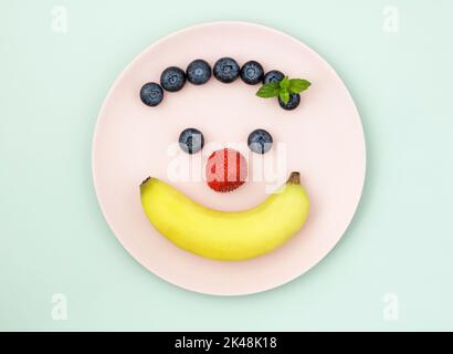 Banane und Beeren auf rosa Teller in der Form eines glücklichen Gesichts angeordnet Stockfoto