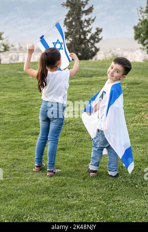 Junge Kinder Mit Israelischer Flagge. Rückansicht Gesichtsloses Kleines Mädchen Und Lächeliger Junge Mit Israel-Flagge Im Park. Go Vote Wahlen Konzept. Präsidentschaftswahlen In Israel. Stockfoto