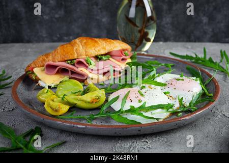 Frühstück mit Spiegeleiern und Croissant-Sandmit Schinken, Käse und Salat. Köstliches Frühstück am Morgen Stockfoto