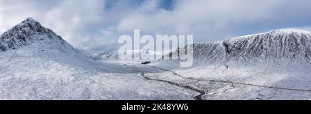 Atemberaubende Luftdrohnen-Panoramaaufnahme von Stob Dearg und Glencoe in den schottischen Highlands bei tiefem Schneefall und schönem blauen Himmel Stockfoto