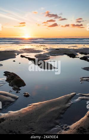 Schönes Landschaftsbild im Sommer bei Sonnenuntergang von Widemouth Bay in Devon England mit goldenem Stundenlicht am Strand Stockfoto