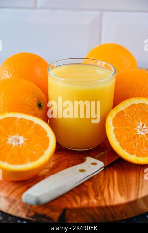 Orangensaftgetränk mit ganzen und geschnittenen Orangen auf Holzschneidebrett Stockfoto