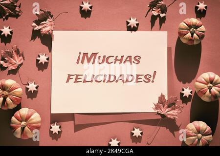 Dekorativer Rahmen mit braunen und orangen Herbstdekor. Kürbisse, Sternkekse und trockene Herbstblätter. Text Muchas Felicidades bedeutet Glückwünsche in span Stockfoto