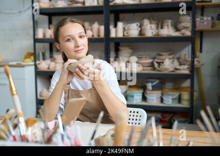 Die Frau hält einen Tonrohling für eine Tasse in ihren Händen Stockfoto