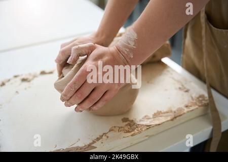 Frau knetet ein Stück Ton mit den Händen auf dem Tisch Stockfoto