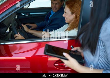 Angenehmes Paar, das Innenwagen von innen im Autozentrum testet Stockfoto
